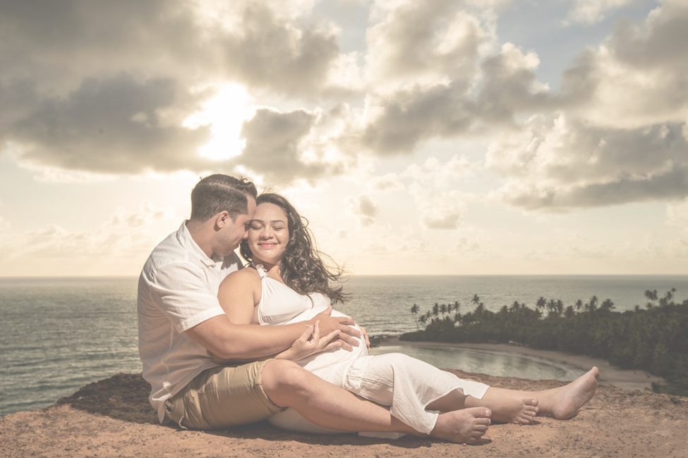 a couple expecting a child sitting near the coastal cliff.