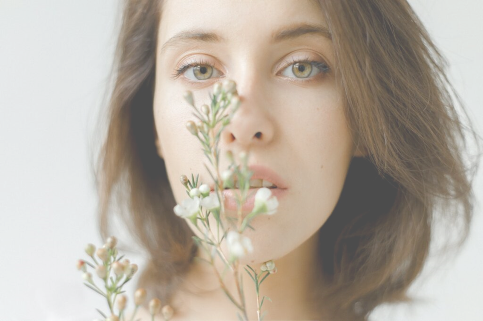 woman with a solemn look holding a flower in front of her face