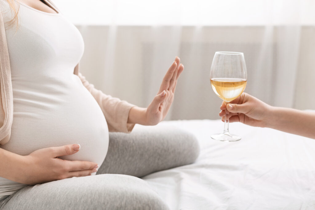 No alcohol during pregnancy. Young pregnant woman refuses to drink wine, making stop gesture to glass, free space
