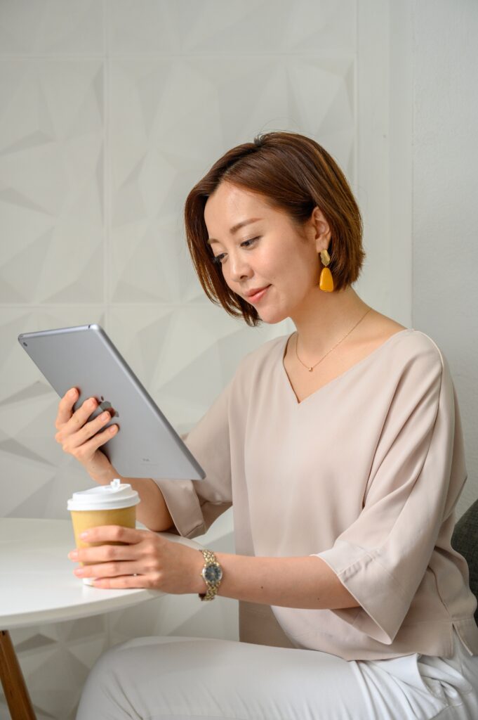 Woman sitting at table, looking at iPad and drinking a cup of coffee.