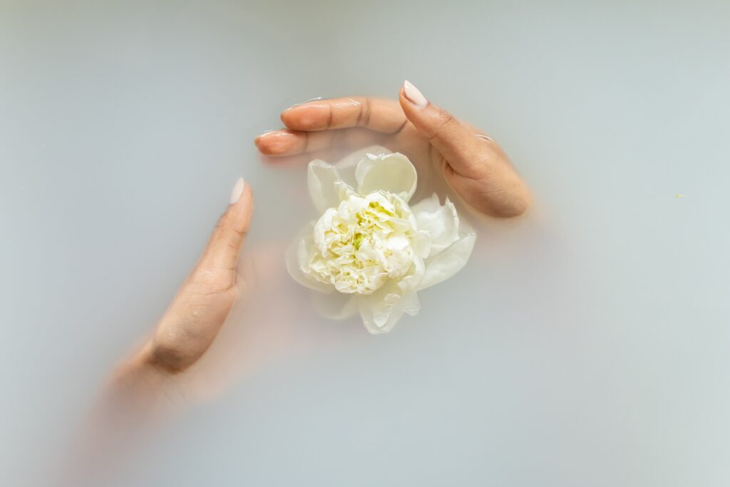 Woman's hands holding flower in bath water.