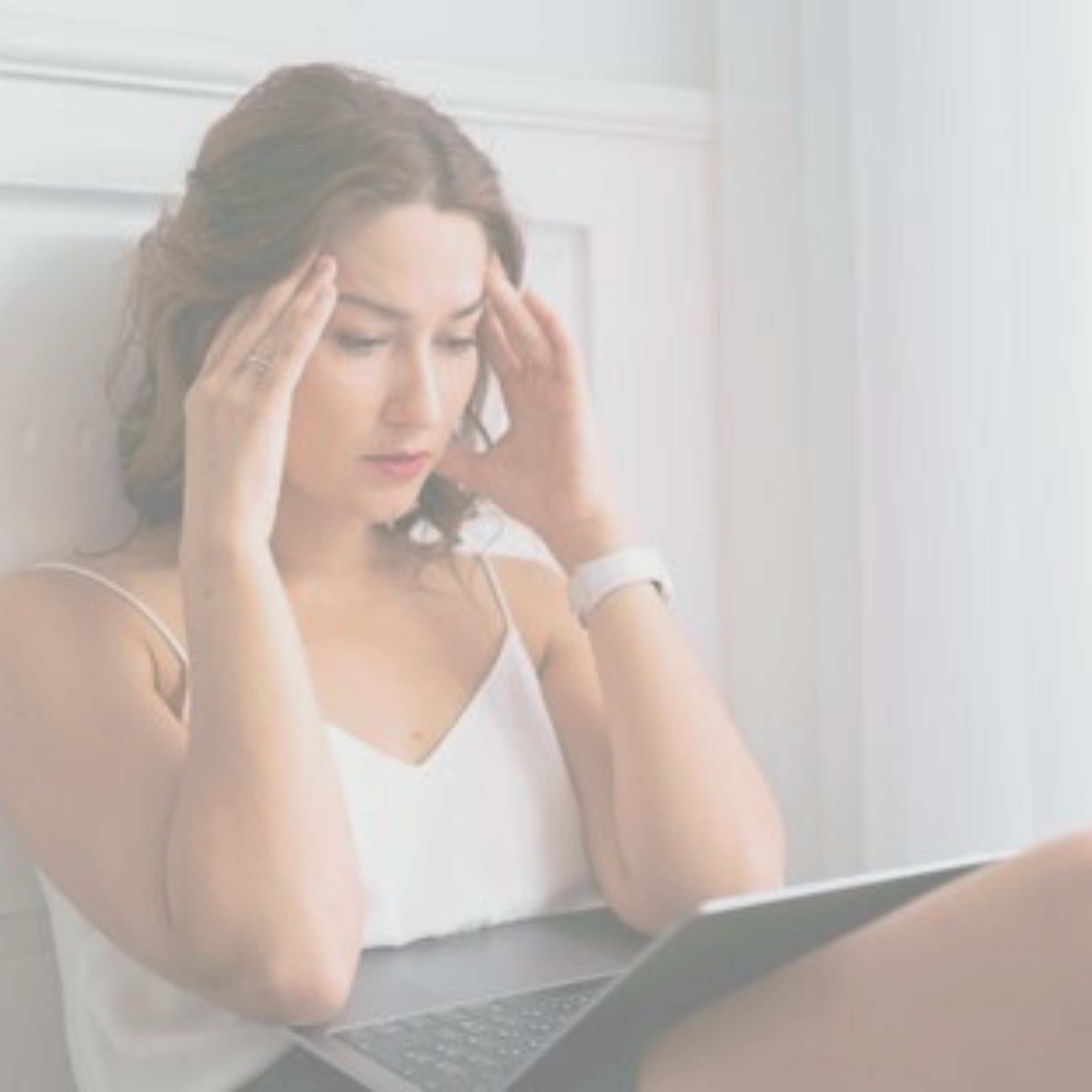 woman sitting on floor with laptop on knees and fingers on temples