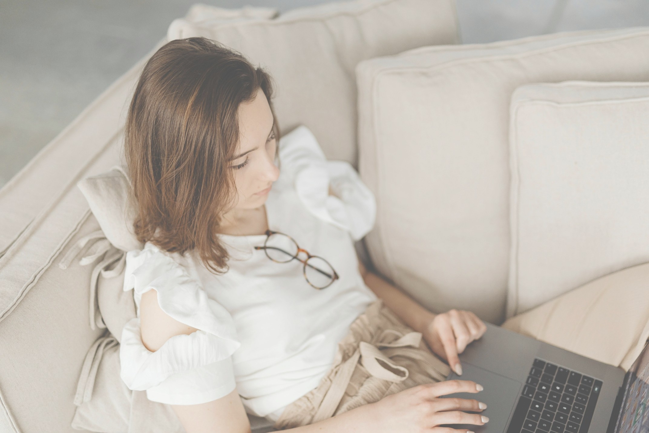 woman wear white shirt sitting on beige sofa while working on her laptop